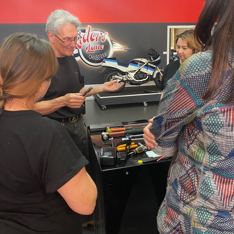 man showing several women motocycle parts with Riders lane sign in background